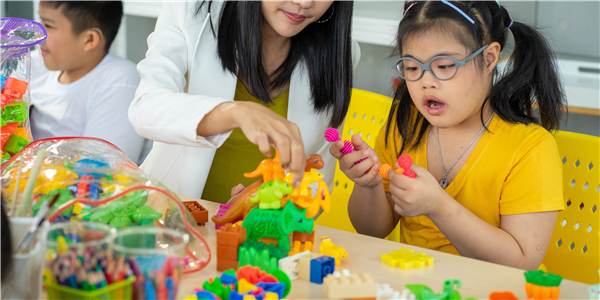 Student with yellow shirt playing with animal manipulatives with teacher present with other student in white shirt.